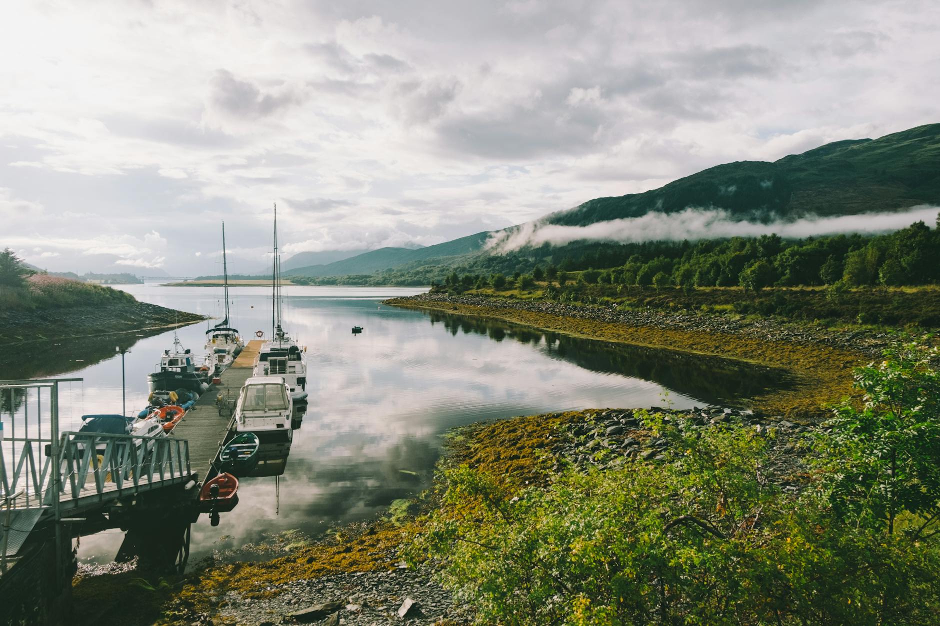 Pomost z łodziami nad spokojnym szkockim jeziorem w górzystym krajobrazie